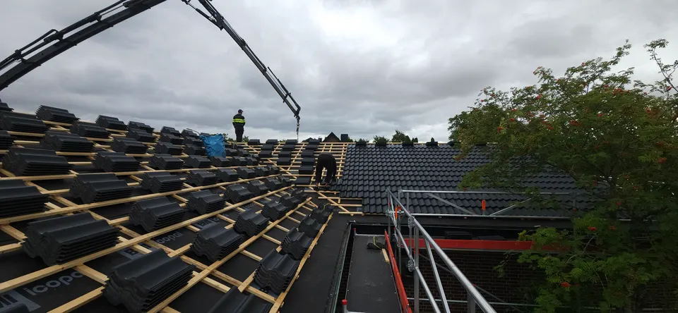 Kranbil lyfter upp betongpannor till taket i Lund